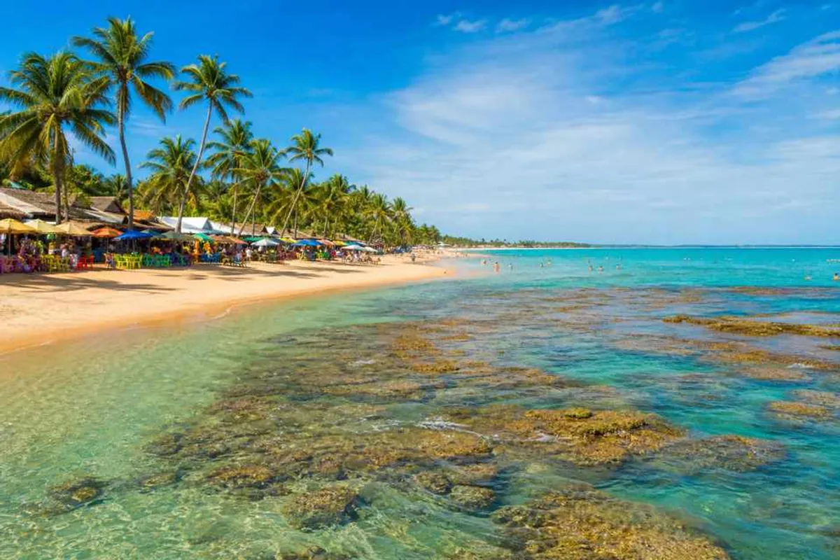 Praia de Porto Seguro na Bahia com coqueiros, mar calmo e barracas